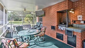Un patio al aire libre con zona de barbacoa de ladrillo, asientos y una pantalla de televisión.