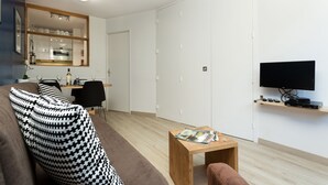 Un soggiorno moderno con un divano, un tavolino, una televisione e una zona cucina visibile tramite una parete divisoria in vetro.
