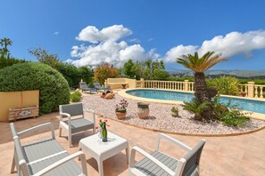 A poolside area with lounge chairs, a table with a bottle and glasses, and a view of the pool and mountains. - Large and comfortable villa in Javea, on the Costa Blanca, Spain  with private pool for 6 persons (Javea)