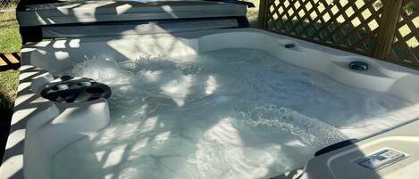 A hot tub with water jets, surrounded by a wooden deck and a lattice fence.