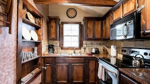 Una cocina con armarios de madera, microondas, horno y un reloj en la pared.
