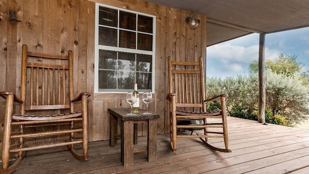 Un porche de madera con dos mecedoras y una mesa, una ventana y vistas a árboles.