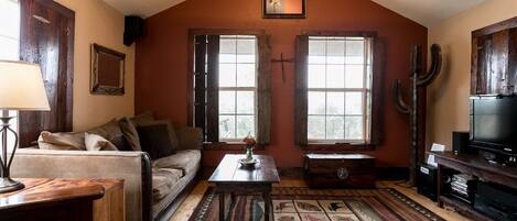A cozy living room with a wooden ceiling, a sofa, a coffee table, a television, and a large window.