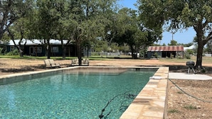 Una piscina cristalina con bordes de piedra, rodeada de árboles y una parrilla.
