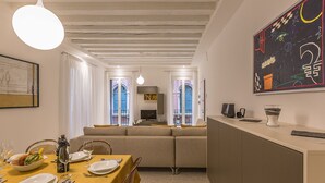 A modern living room with a sofa, dining table set for two, and a kitchen area with a counter and appliances. - Ca' Rossini 1 Apartment (Venice)
