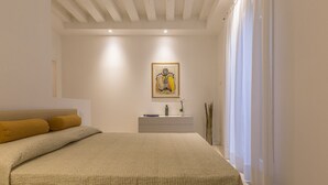 A bedroom with a large bed, a bedside table with a plant, and a framed artwork on the wall. - Ca' Rossini 1 Apartment (Venice)