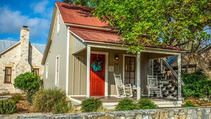 A stone house with a red door, a porch with white chairs, and a stone wall in front. - Das Solheid Sunday House | Close to Main (Fredricksburg)