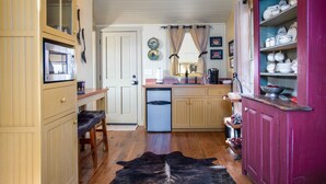 A compact kitchen with wooden cabinets, a refrigerator, a sink, and a dining area with a bench. - Das Solheid Sunday House | Close to Main (Fredricksburg)