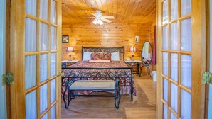 A wooden cabin bedroom with a bed, bedside tables, a desk, and a ceiling fan. - Ladybug Resort Romantic Cabin with Mountain Views (Sevierville)