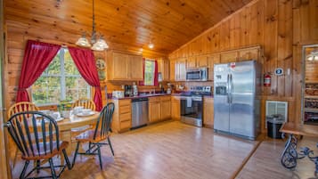 A wooden cabin kitchen with a dining table, chairs, a refrigerator, a microwave, and a dishwasher.