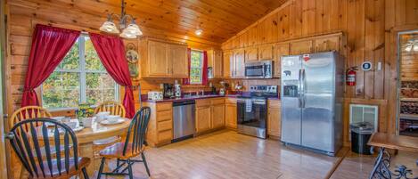 A wooden cabin kitchen with a dining table, chairs, a refrigerator, a microwave, and a dishwasher.