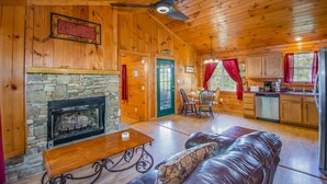 A cozy cabin interior with a stone fireplace, wooden walls, a dining area, and a kitchen. - Ladybug Resort Romantic Cabin with Mountain Views (Sevierville)