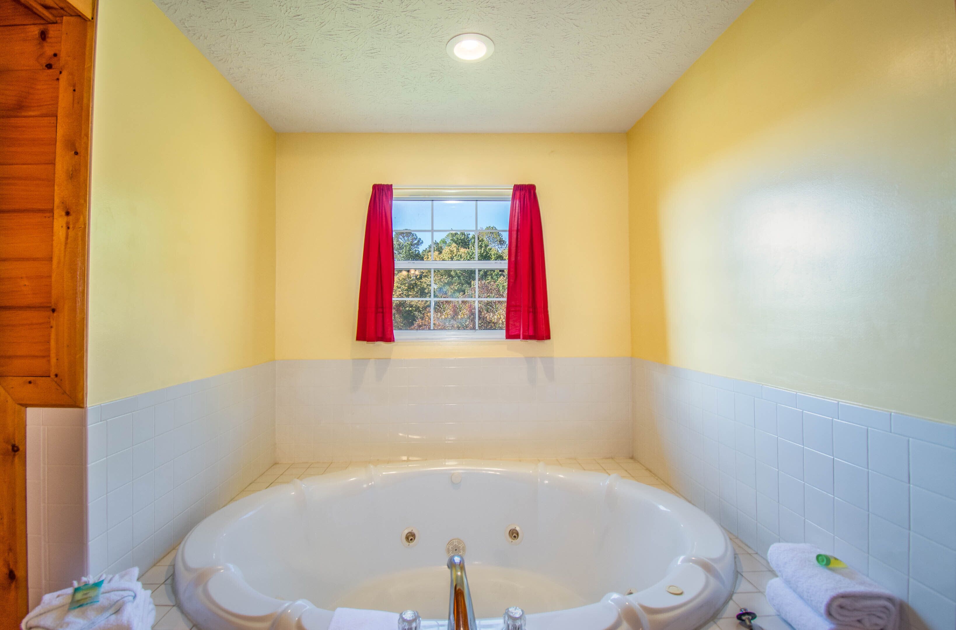 A bathroom with a bathtub, a window with red curtains, and a wooden door.
