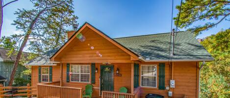 A log cabin with a porch, green chairs, and a trash bin.