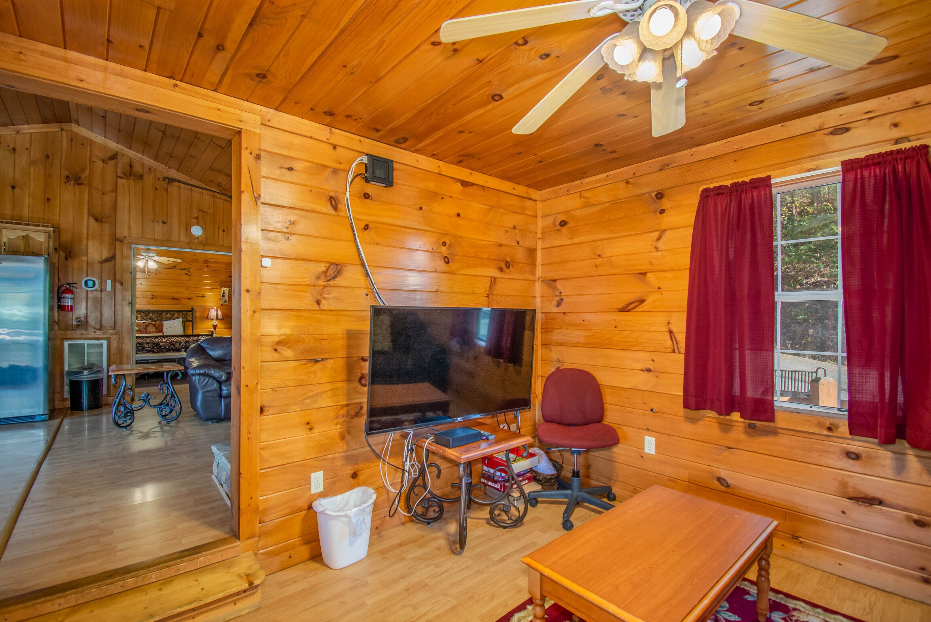 A wooden cabin interior with a television, a red chair, and a table.