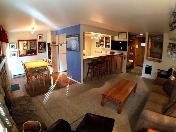Cozy living space with a dining table, sofa, and kitchen area featuring a refrigerator, sink, and bar with stools.
