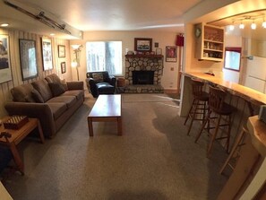 Cozy living room with a fireplace, sofa, and coffee table, featuring a bar area with stools.
