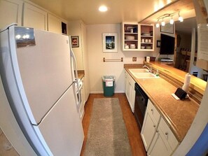 Compact kitchen with refrigerator, sink, and countertop, featuring a trash bin and cabinets.