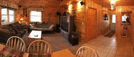 A cozy cabin interior with a wooden interior, a sofa, a television, and a dining area with chairs and a table.
