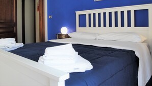 A neatly made bed with white linens and a blue headboard. There is a painting on the wall above the bed and a wooden door to the left. - Umberto I Holiday House (Napoli)