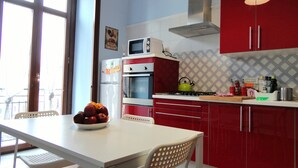 A kitchen with red cabinets, a white table, and a bowl of fruit. - Umberto I Holiday House (Napoli)