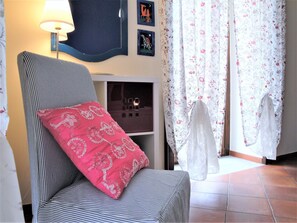 Una habitación con un sillón a rayas, un cojín decorativo rosa, una lámpara de pared y una cortina estampada.
