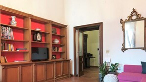 A living room with a wooden entertainment unit, a television, a pink sofa, and a mirror on the wall. - Umberto I Holiday House (Napoli)