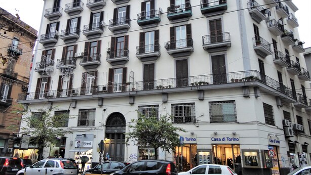 A multi-story building with balconies, storefronts, and parked cars. - Umberto I Holiday House (Napoli)