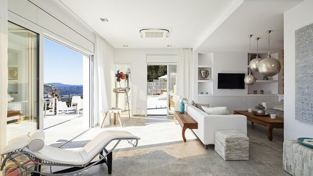 Una sala de estar moderna con una tumbona, un sofá y un televisor. Hay una ventana grande con vistas al exterior.