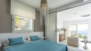 Un dormitorio moderno con una cama grande, una araña, vistas a un balcón y una puerta corredera que da al baño.