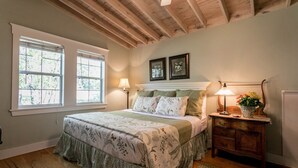 Une chambre à coucher avec un grand lit, deux lampes de chevet, une commode et une fenêtre avec des stores.