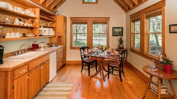 Une cuisine chaleureuse avec des meubles en bois, une table à manger pour quatre personnes et de grandes fenêtres donnant sur l’extérieur.