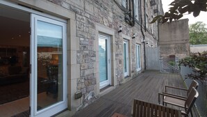 A stone building with large glass doors and windows, a wooden deck with benches, and a small outdoor area with a railing.