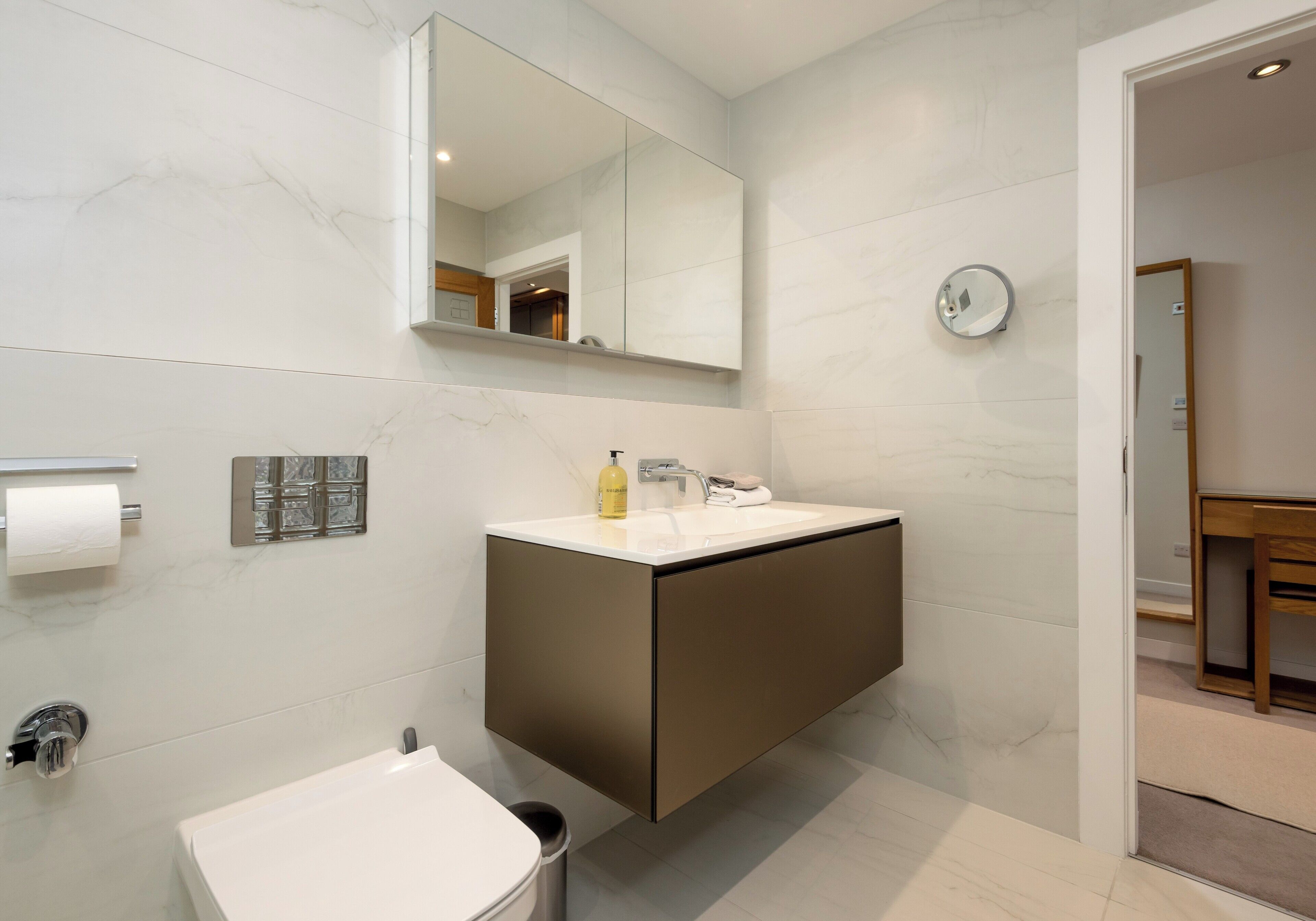 A modern bathroom with a marble wall, a built-in sink, a mirror, and a toilet.