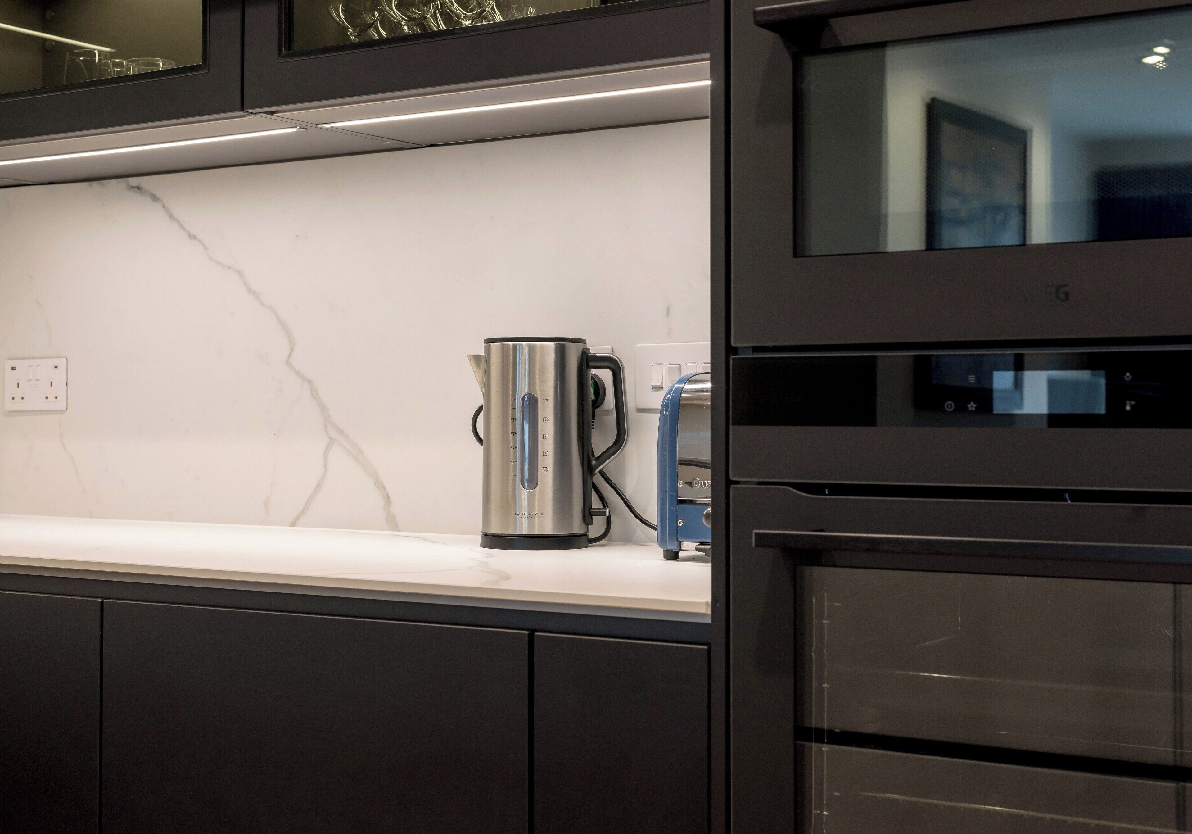 A modern kitchen with a marble countertop, a stainless steel kettle, and a built-in oven.