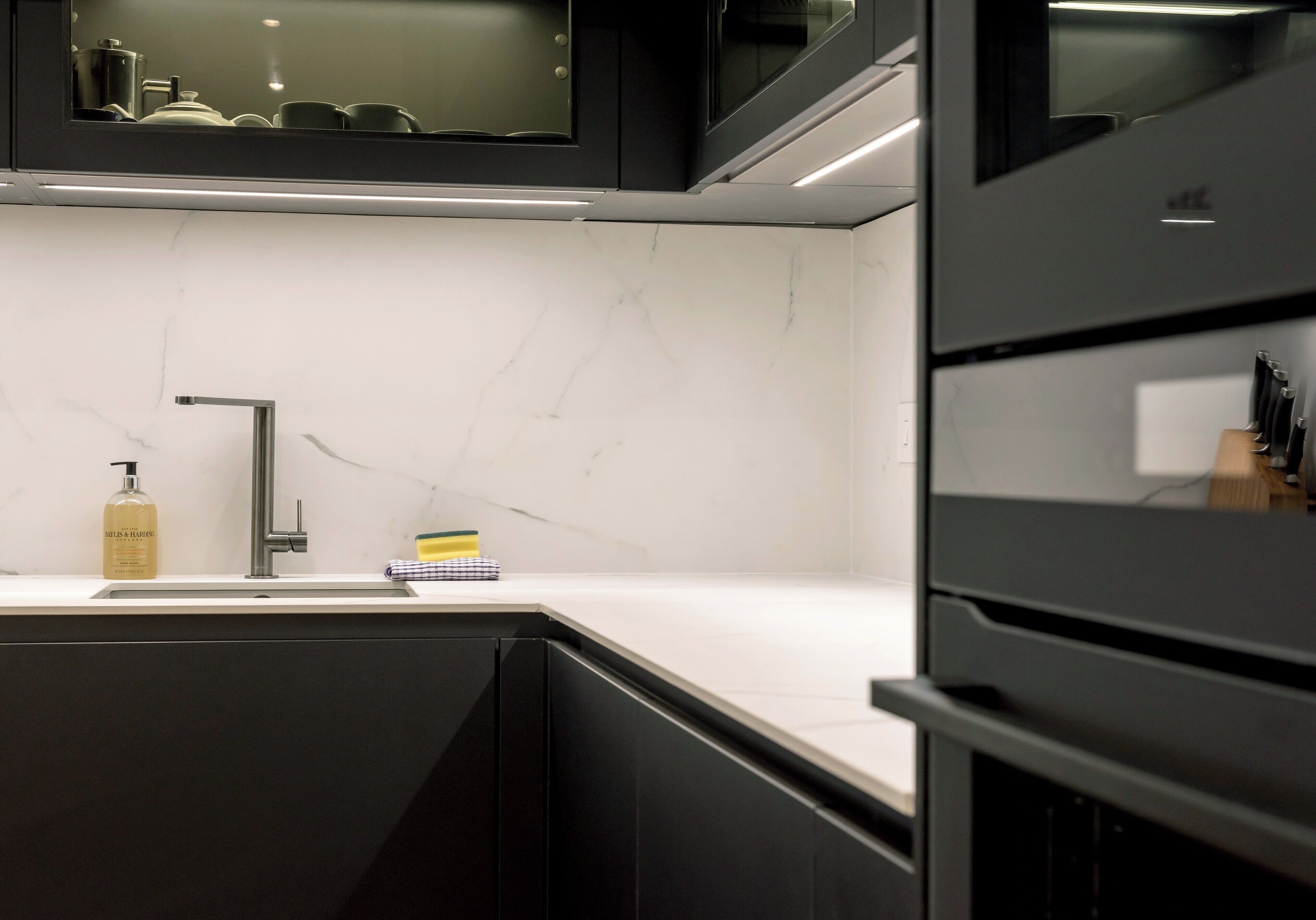 A modern kitchen with a marble countertop, a stainless steel sink, and black cabinetry.