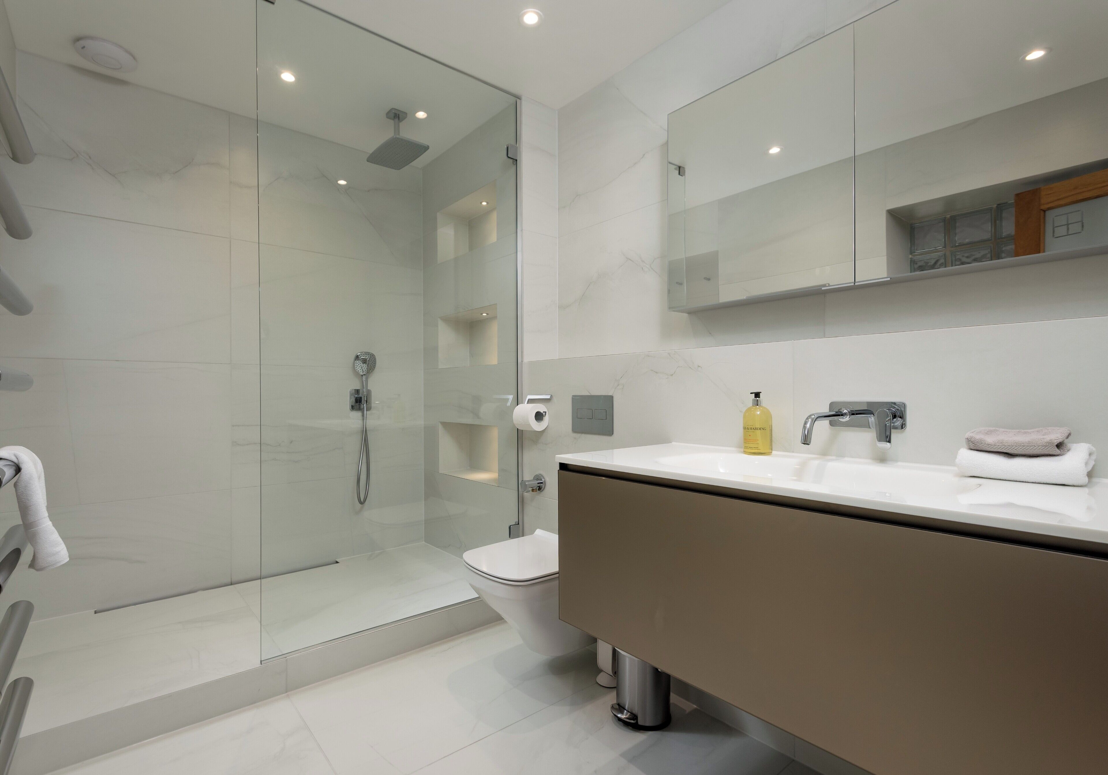 A modern bathroom with a glass-enclosed shower, a toilet, a sink with a mirror, and a towel rack.