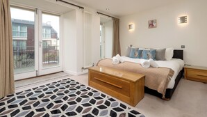 A bedroom with a large bed, a wooden bench, a bedside table, and a view through a sliding door to the outside.
