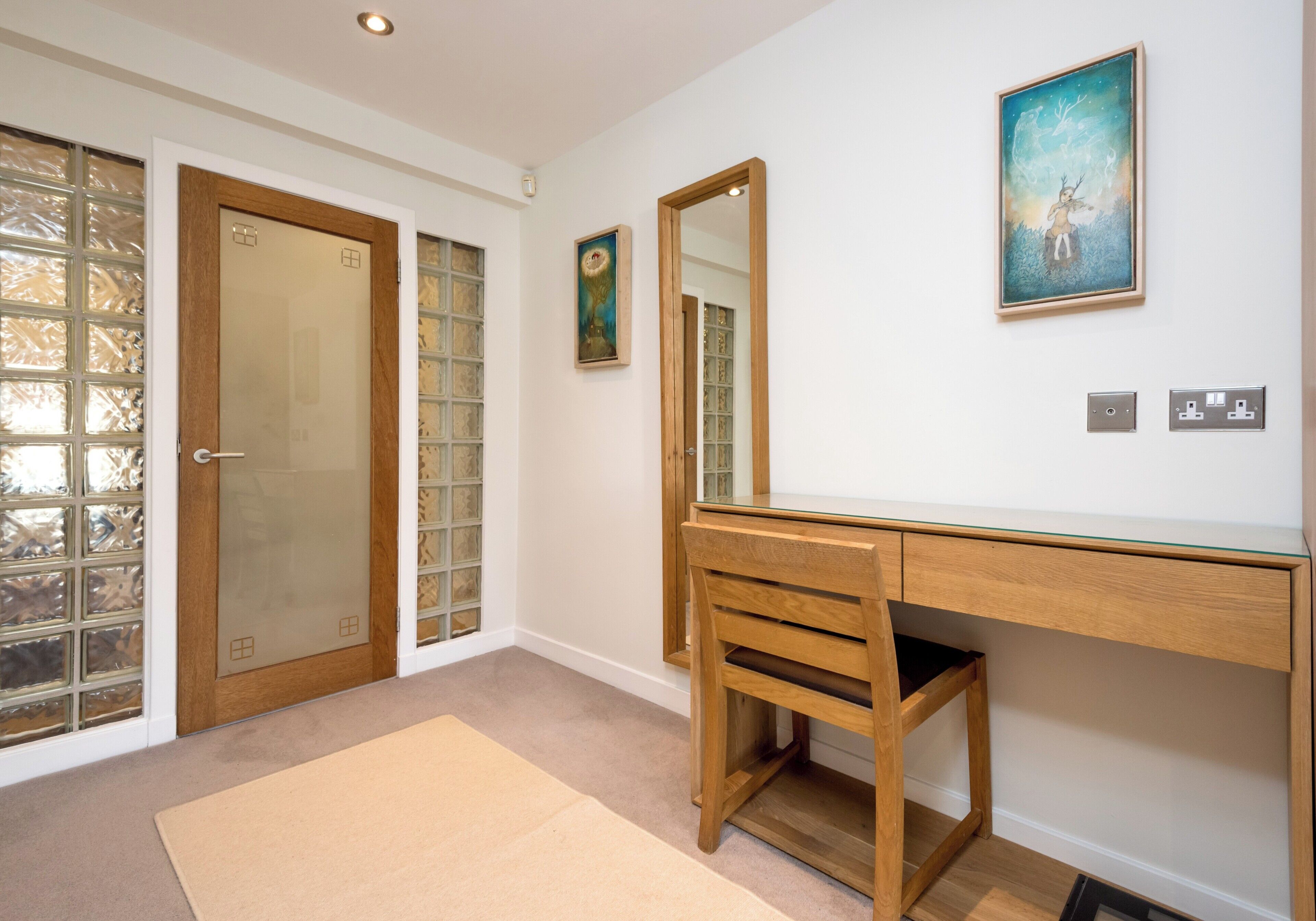 A room with a wooden desk, a chair, a large mirror, a framed painting, and a door with frosted glass panels.
