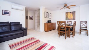 Un salon avec un canapé en cuir noir, un tapis à rayures, une table à manger en bois avec des chaises et un ventilateur de plafond.
