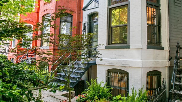 Une rangée de maisons de ville à trois étages, chacune ayant un petit jardin devant.
