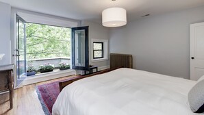 Une chambre avec un grand lit, une fenêtre donnant sur un espace verdoyant, un radiateur et une porte.
