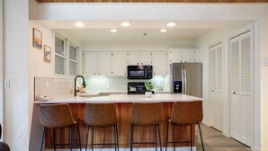 A modern kitchen with white cabinets, a central island with bar stools, a microwave, a refrigerator, and a coffee machine. - CX212 | Amazing Property | Ski In/Out | Winter Shuttle | Hot Tub | Pool (Steamboat Springs)