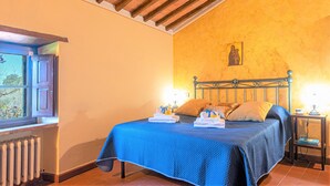 Un dormitori amb un llit, una finestra, un radiador i una paret amb una pintura religiosa.