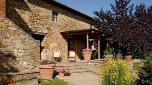 Edifici de pedra amb terrassa coberta, mobiliari exterior i plantes en testos.