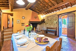 Enjoy meals in this dining area with a long table set for a meal, surrounded by a wooden bench and a stone fireplace.