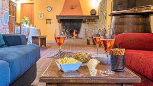 Un saló d'estar acollidor amb una llar de foc, una taula de fusta amb aperitius i begudes, i seients còmodes.