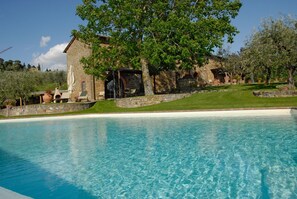Relax by the serene pool surrounded by lush greenery and a rustic stone building.