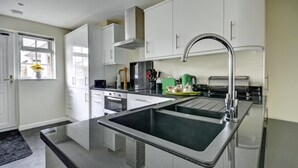 A modern kitchen with white cabinets, stainless steel appliances, and a double sink. - 1 Bed in Northam, Bideford (oc-cedars) (Northam)