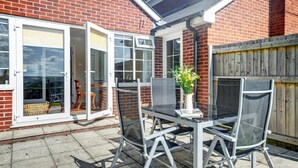 A patio with a glass table and chairs, a wooden fence, and a brick wall. - 1 Bed in Northam, Bideford (oc-cedars) (Northam)